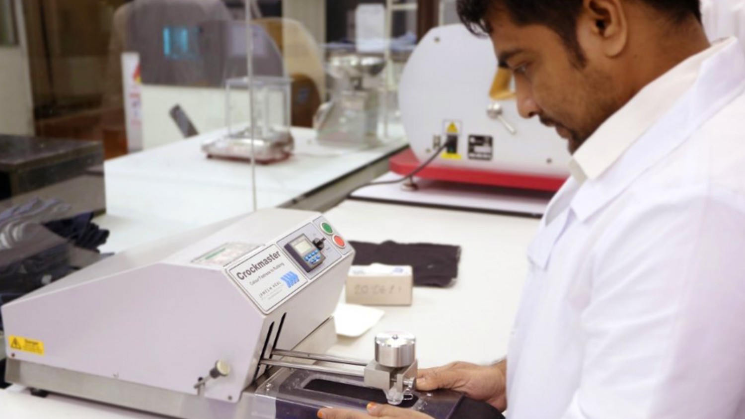 A man in a white lab coat prepares a crockmeter for testing colorfastness of textiles.